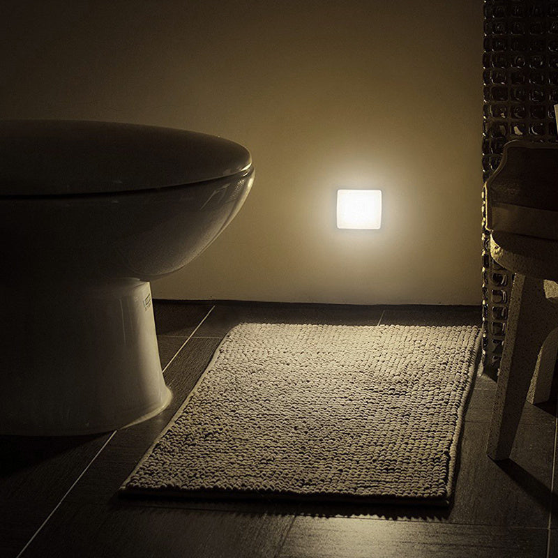 Bathroom with a toilet and rug illuminated by a square light fixture on the wall.