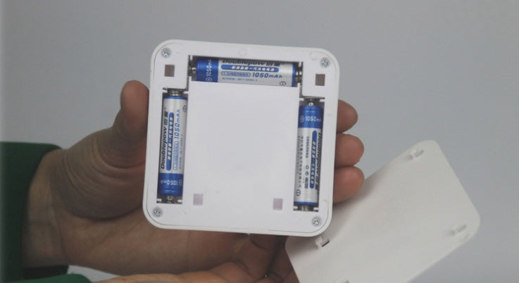Hand holding a small electronic device with batteries inside against a plain background