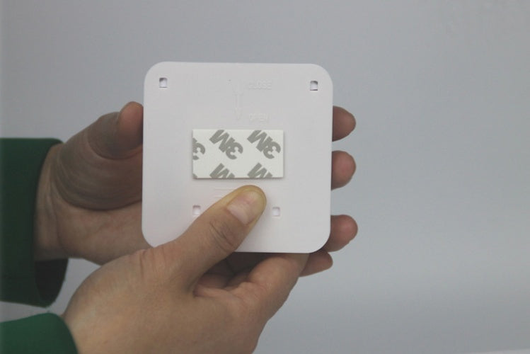 Hand holding a small white square device with a label on a plain background
