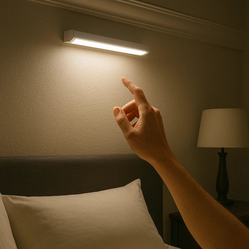 Hand reaching towards a wall-mounted light fixture in a dimly lit room.