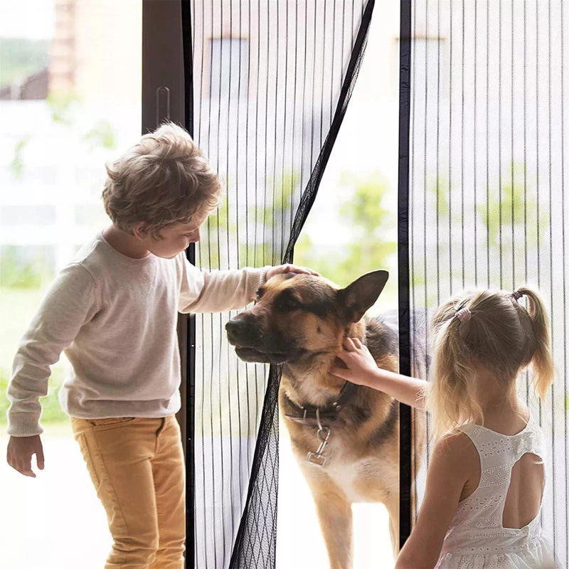 Two children petting a dog through a glass door with a screen.