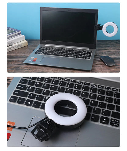 Laptop with a ring light attached on a desk with books and a phone.