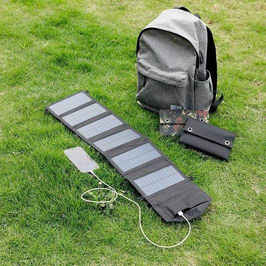 Solar panel charging device on grass with a backpack and small bag nearby